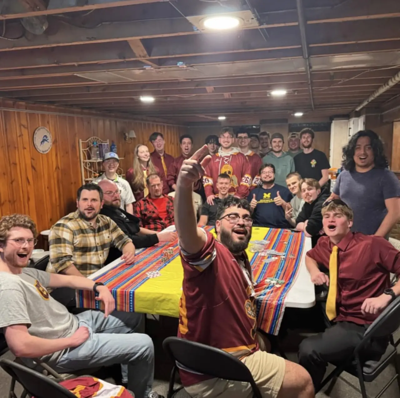 The chapter crowded around a table at a chapter house gathering, several in Theta Tau jerseys.