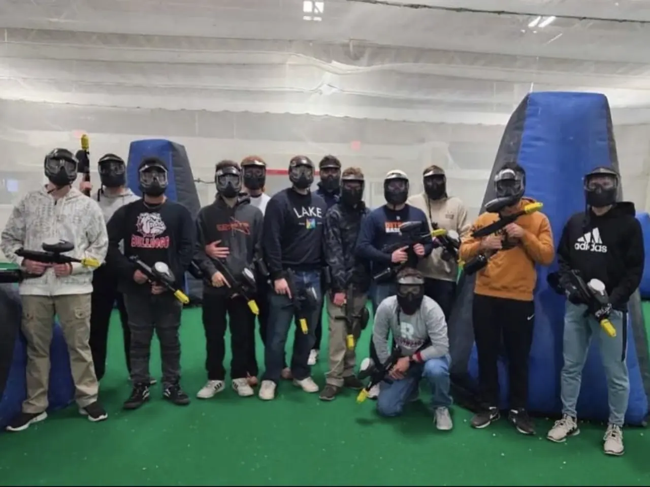 Brothers in masks holding paintball markers at an indoor course.