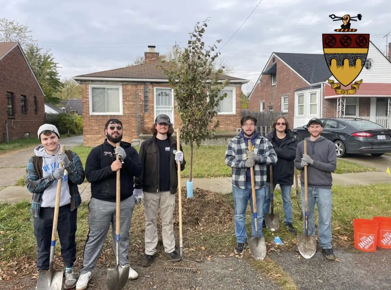 Brothers standing with shovels beside a newly planted tree on a Detroit street.