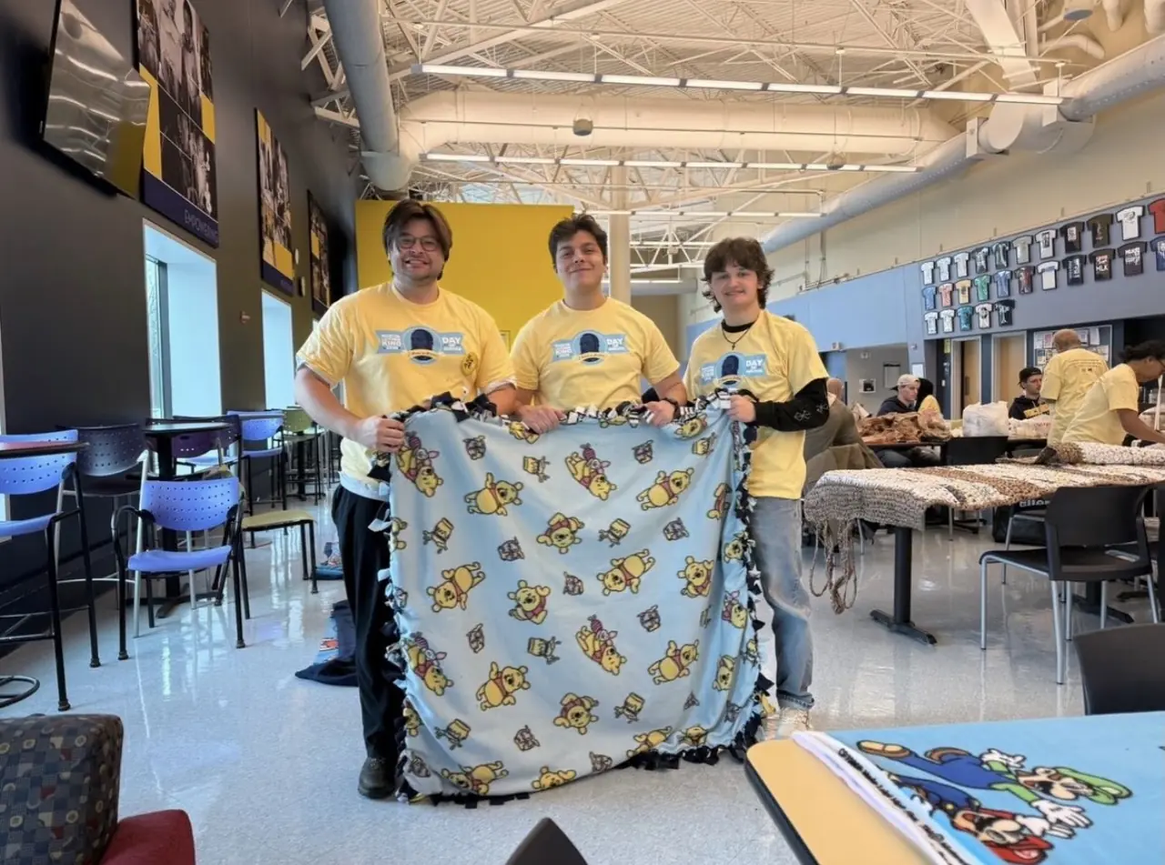 Brothers in Day of Service shirts holding up a fleece blanket they tied.